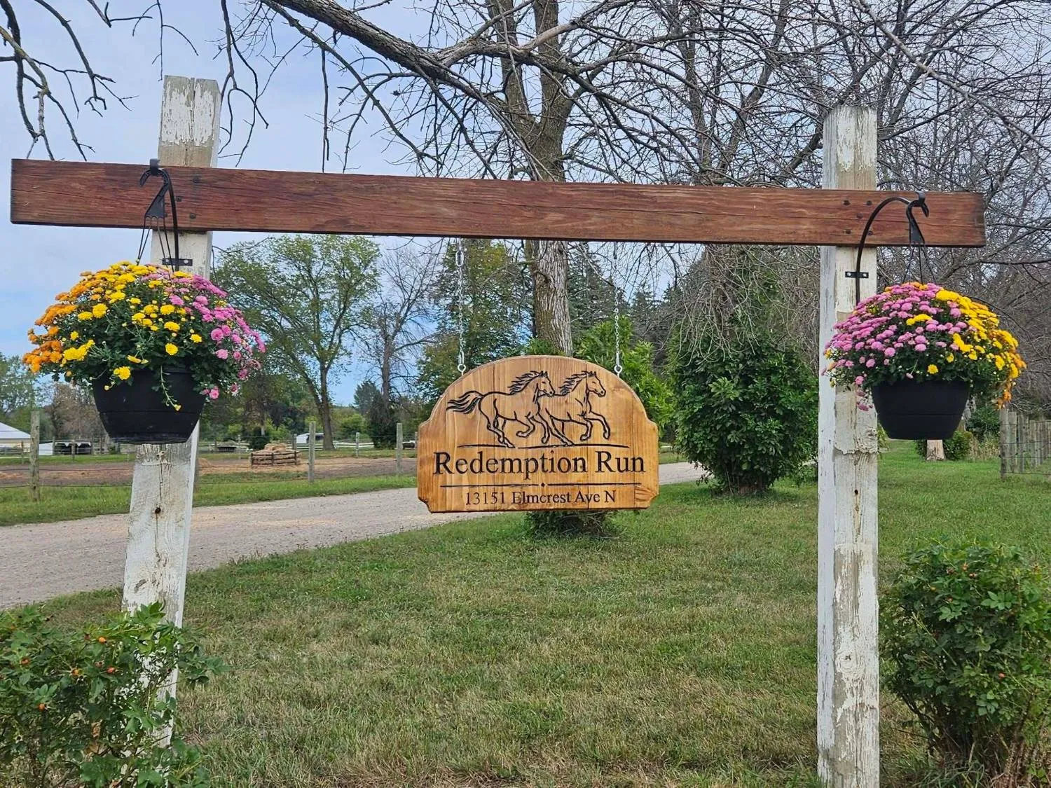 The carved wooden Redemption Run sign at the farm entrance, hung between two baskets of mums