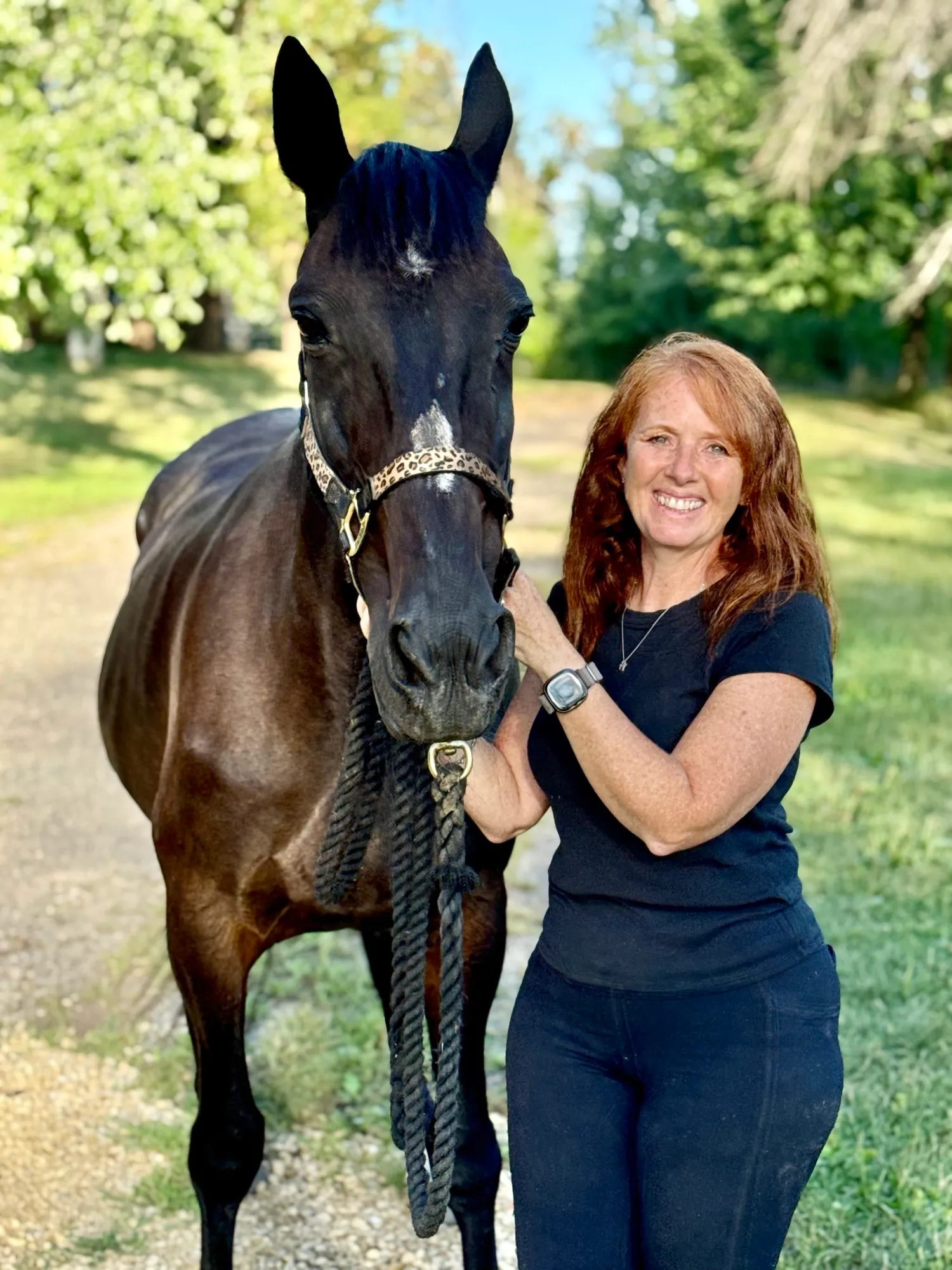 Karrie Cable Rodriquez of Redemption Run smiling beside a dark bay horse in a leopard-print halter